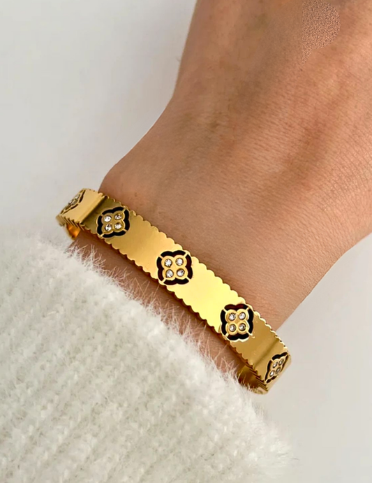 A WOMAN WEARING GOLD PLATED CLOVER BANGLE LAYING ON WHITE SURFACE