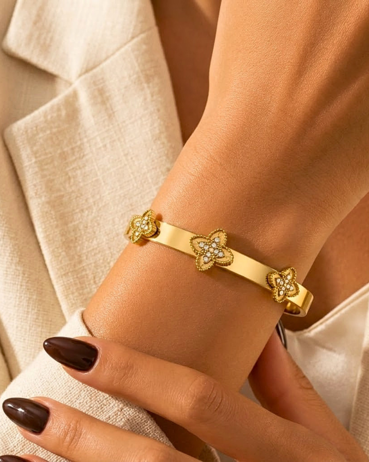 Gold bracelet with floral designs on a wrist against a neutral background