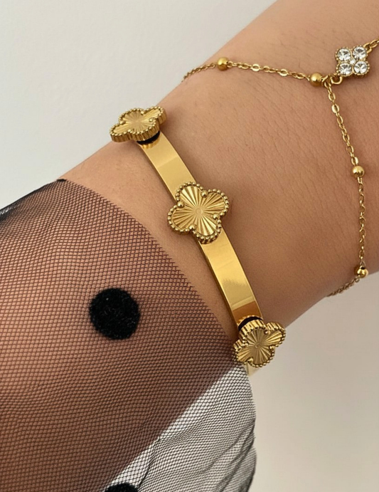 Gold bracelet with decorative elements on a wrist against a neutral background