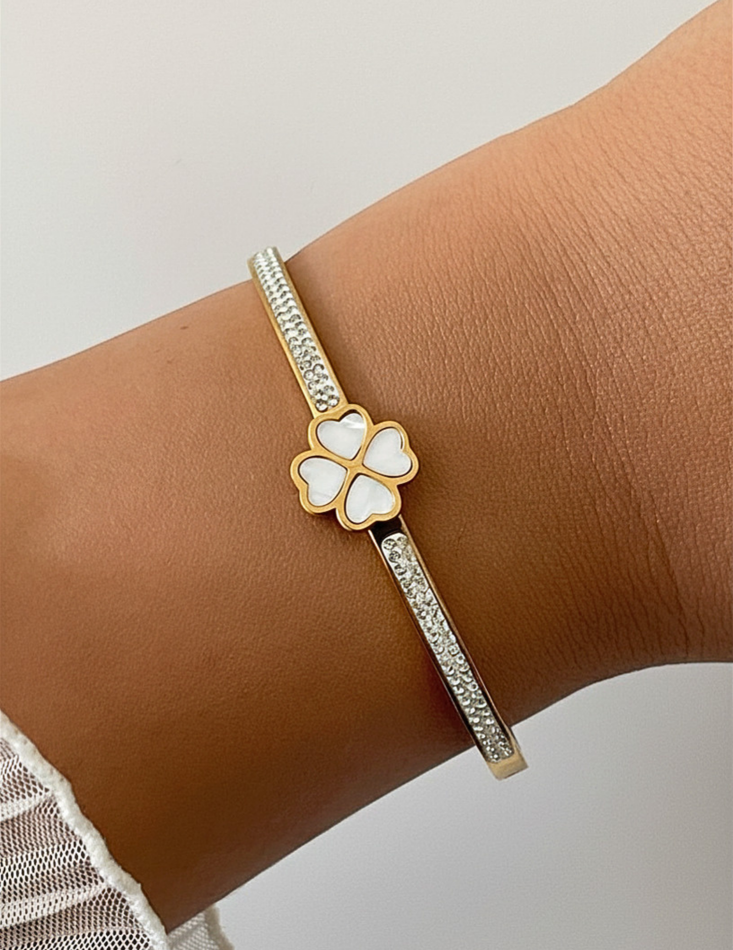 hand wearing gold plated bangle laying on white plain surface