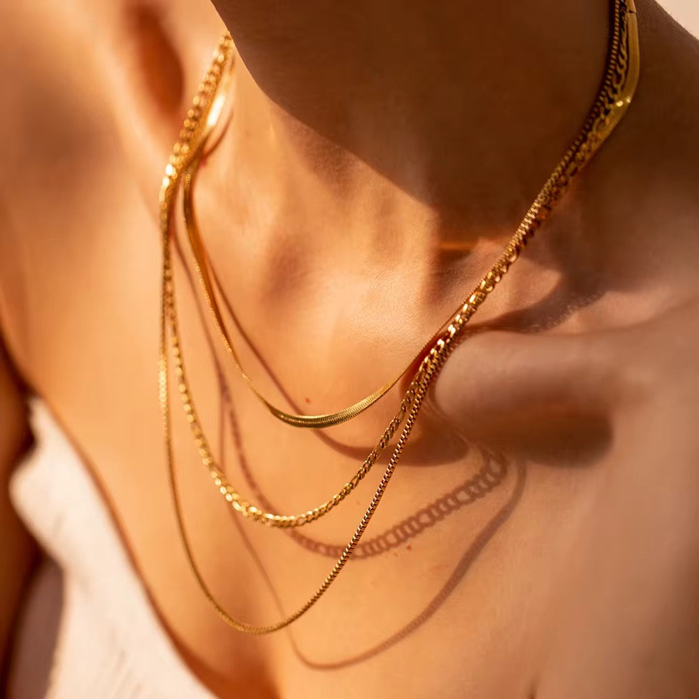 Close-up of a person wearing multiple gold necklaces on a blurred background
