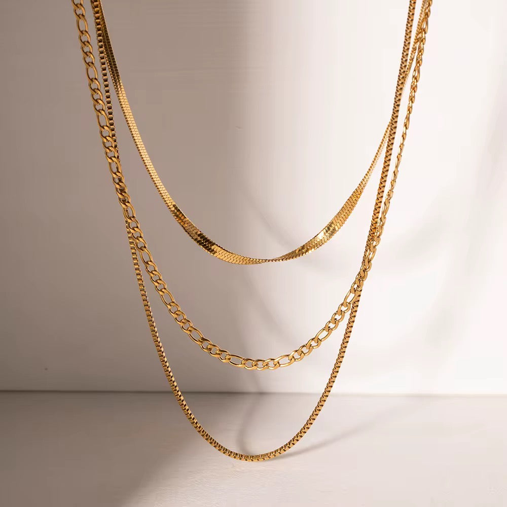Three gold chain necklaces on a neutral background