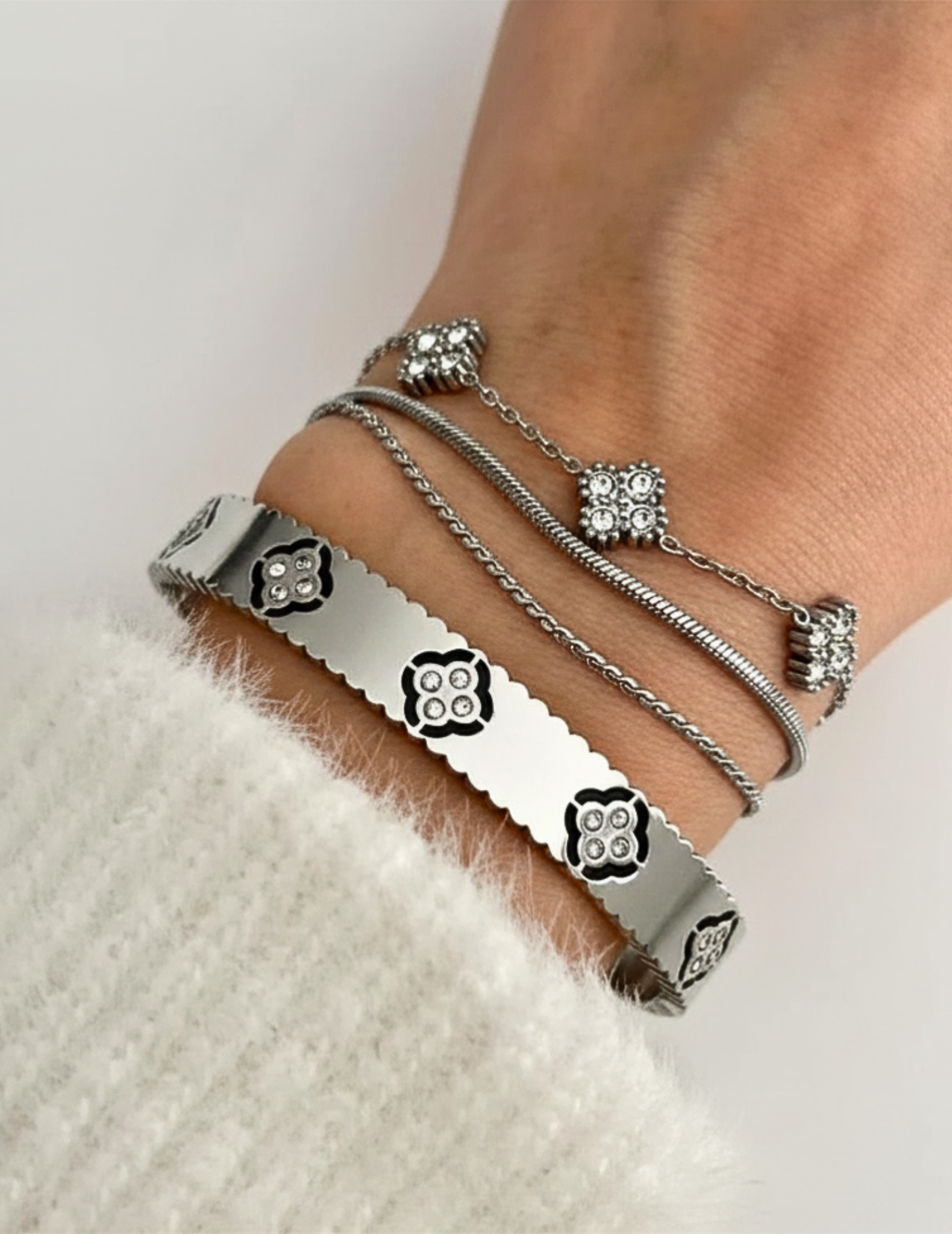 A WOMAN WEARING CLOVER SILVER BANGLE AND TWO OTHE BRACELETS LAYING ON WHITE SURFACE