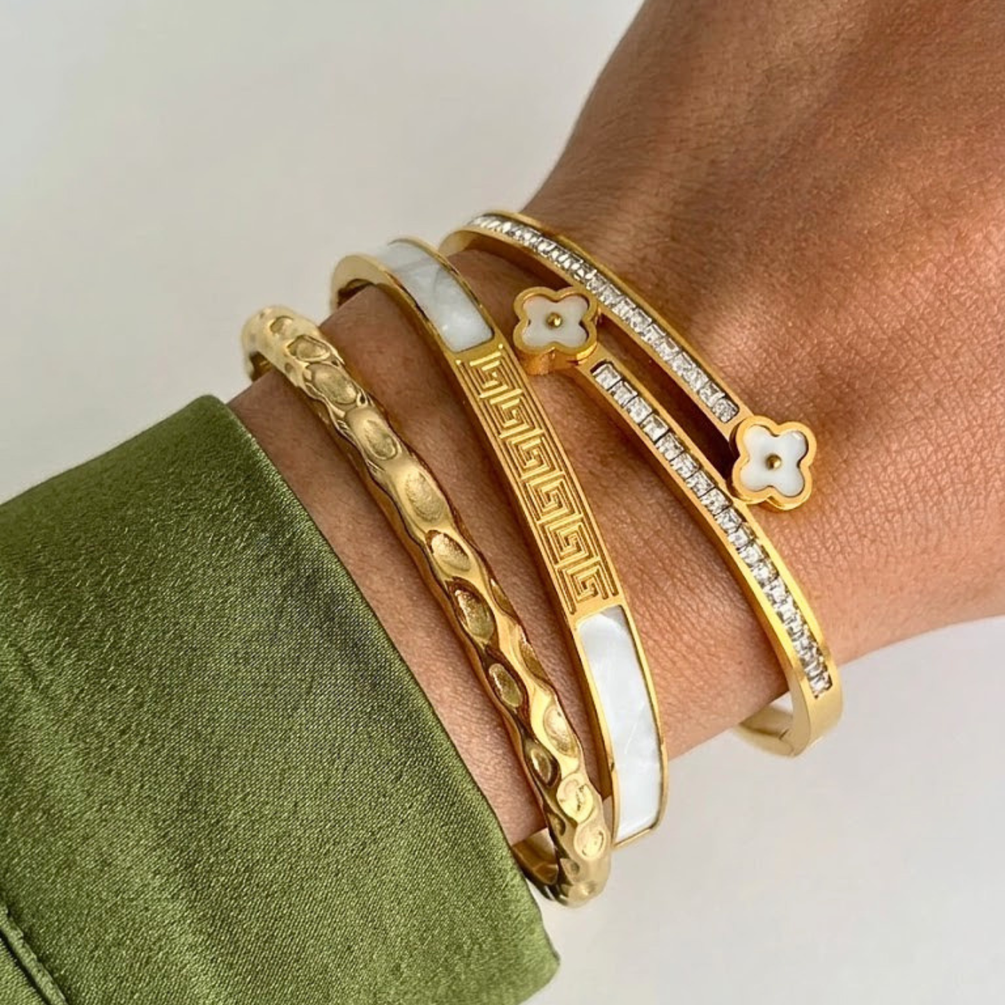 Gold bracelets on a wrist with a green fabric background