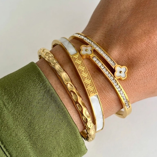 Gold bracelets on a wrist with a green fabric background