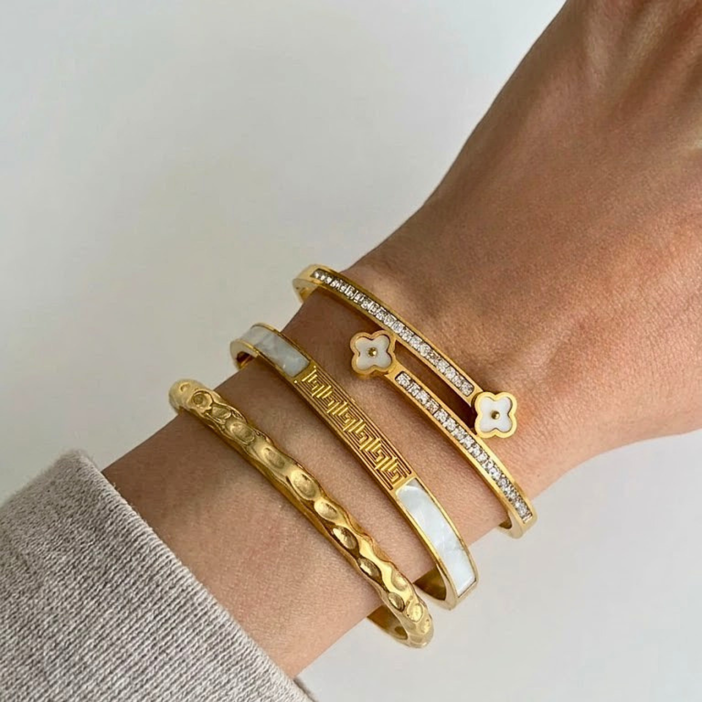 Gold bracelets on a wrist with a neutral background