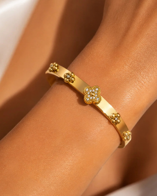 Gold bracelet with floral designs on a wrist against a neutral background