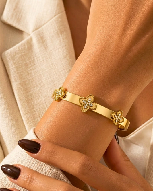 Gold bracelet with floral designs on a wrist against a neutral background