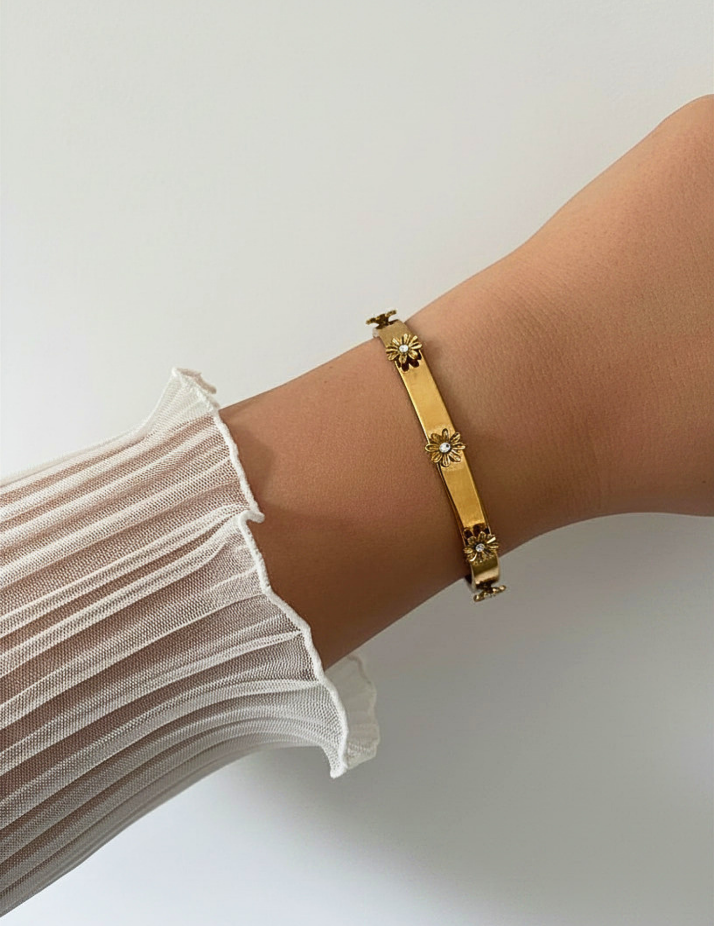 wrist wearing gold bangle on neutral background