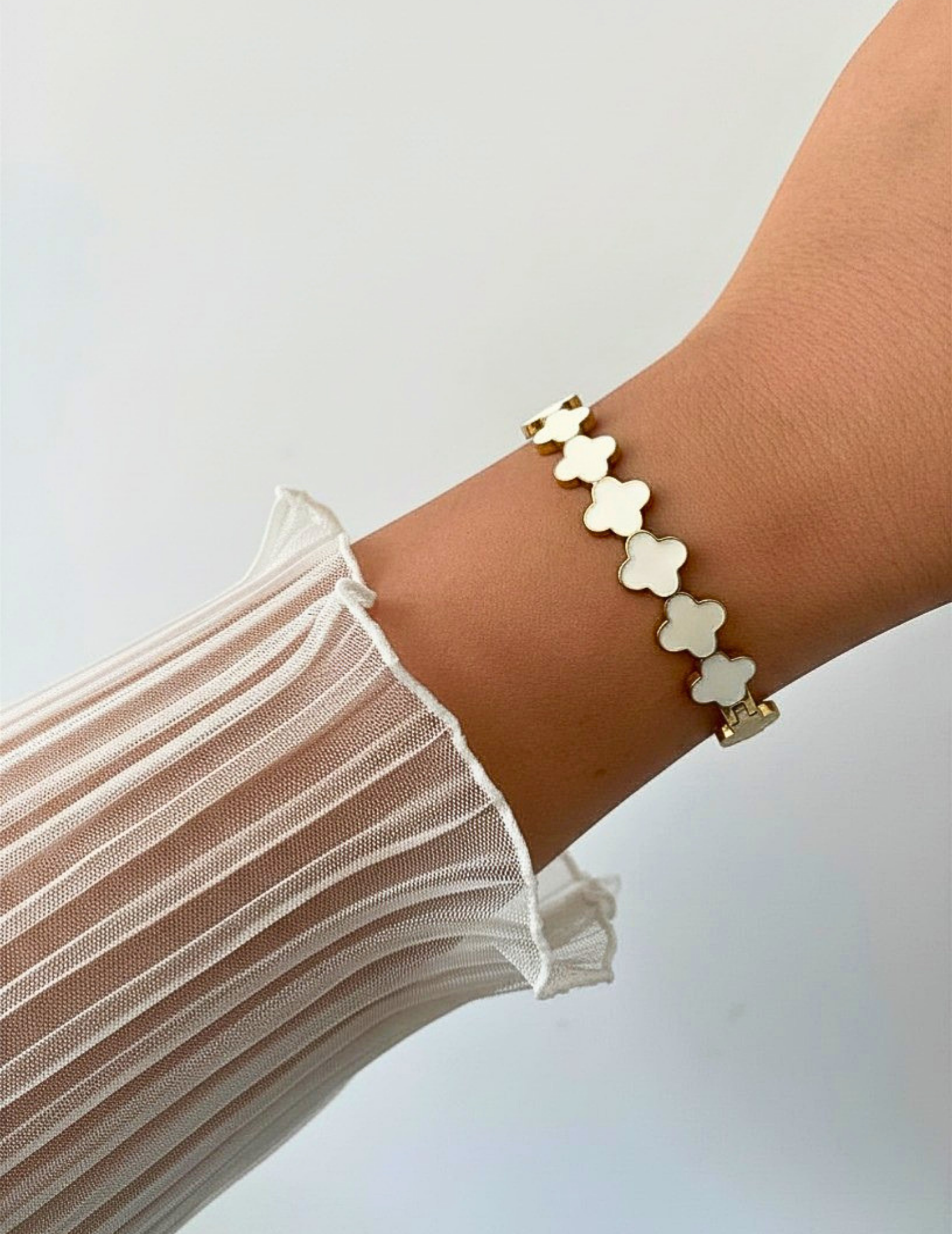 Wrist wearing a white clover bangle on a neutral background.