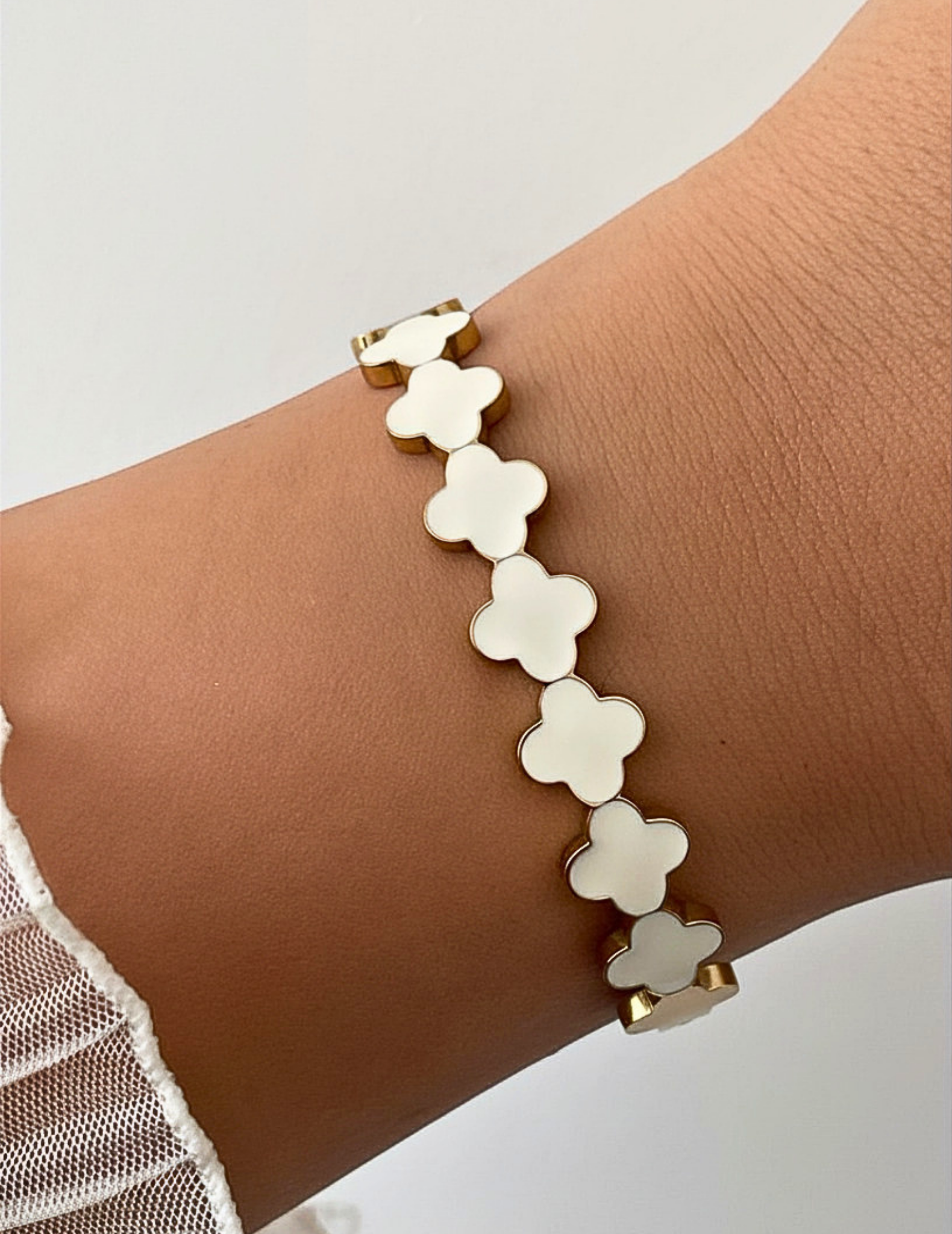 Wrist wearing a white clover bangle on a neutral background.
