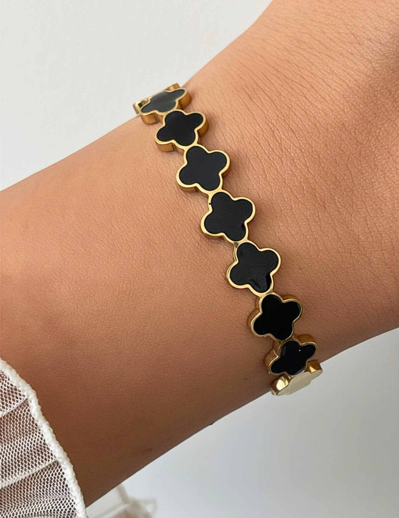 Wrist wearing a black clover bangle on a neutral background.