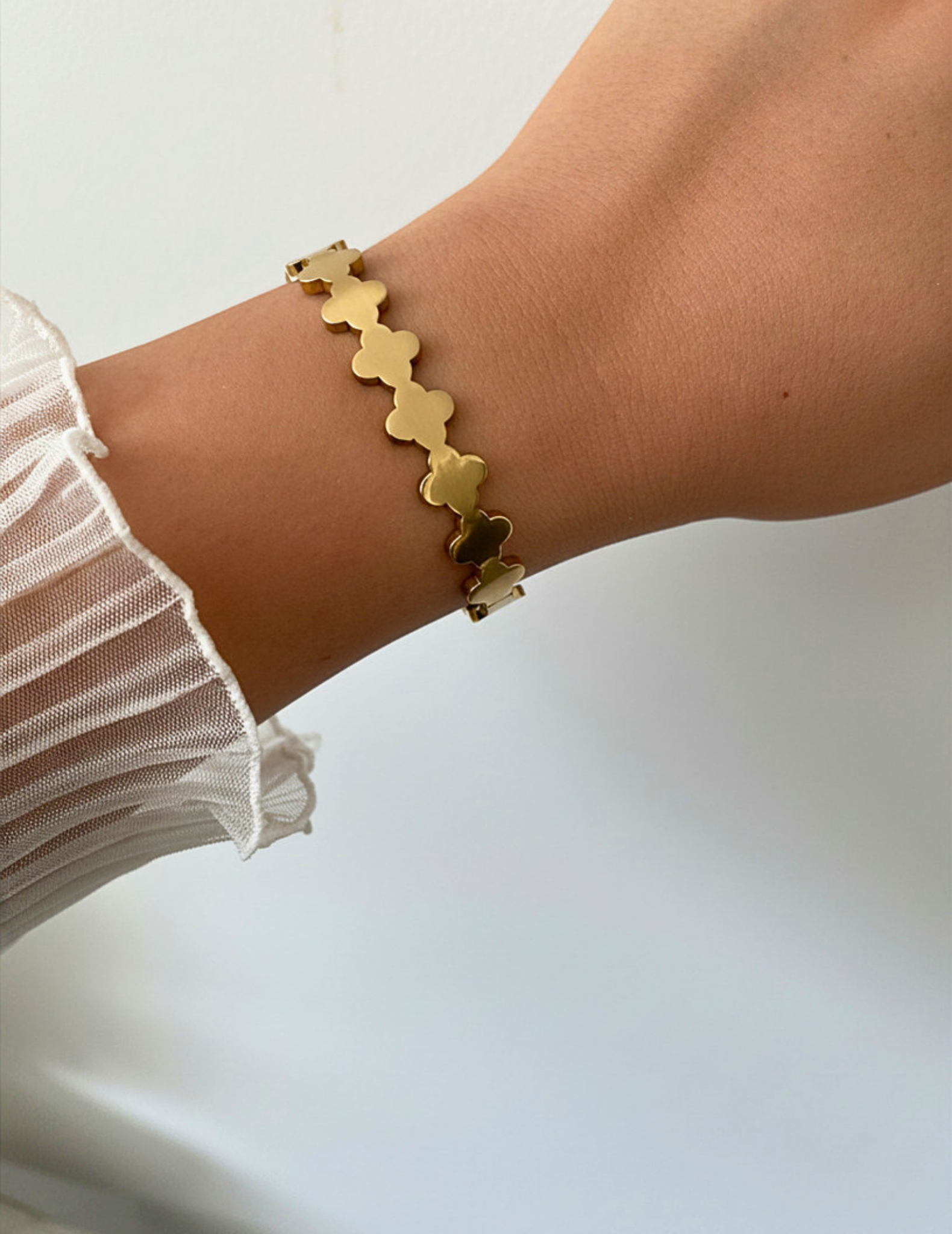 Wrist wearing a gold clover bangle on a neutral background.