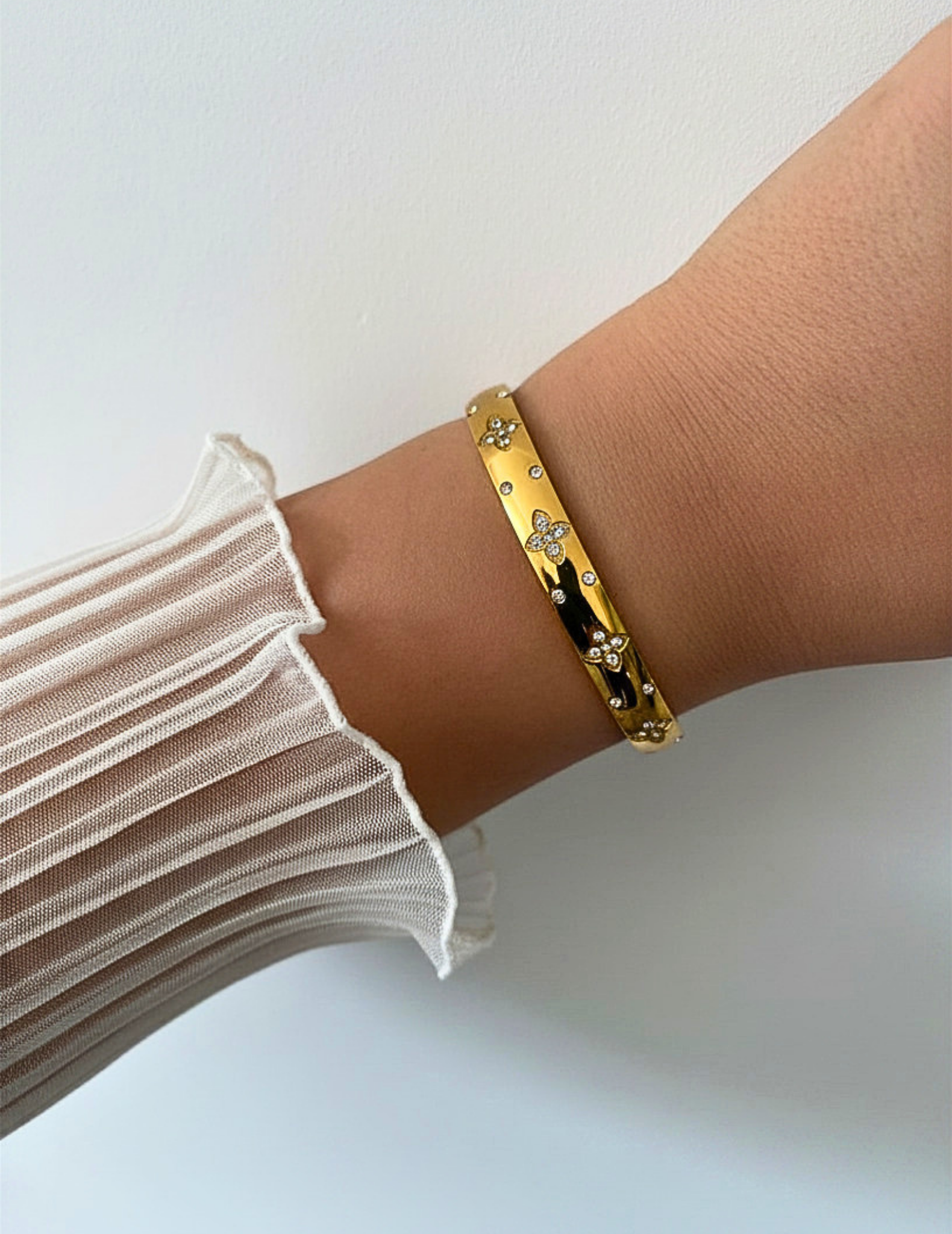 wrist wearing gold bangle on neutral background