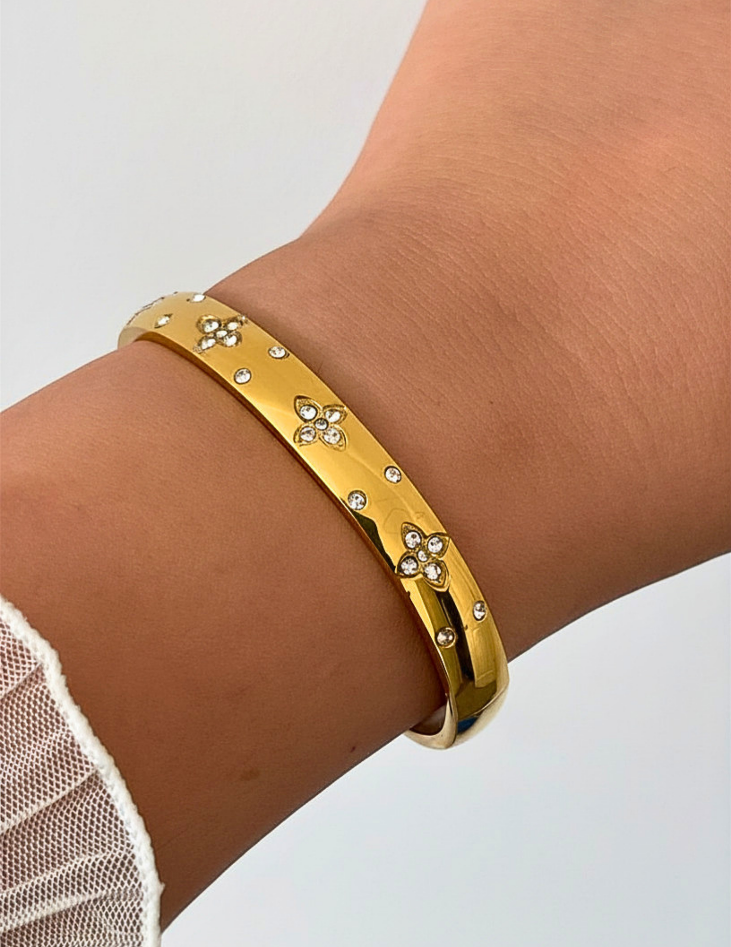 wrist wearing gold bangle on neutral background