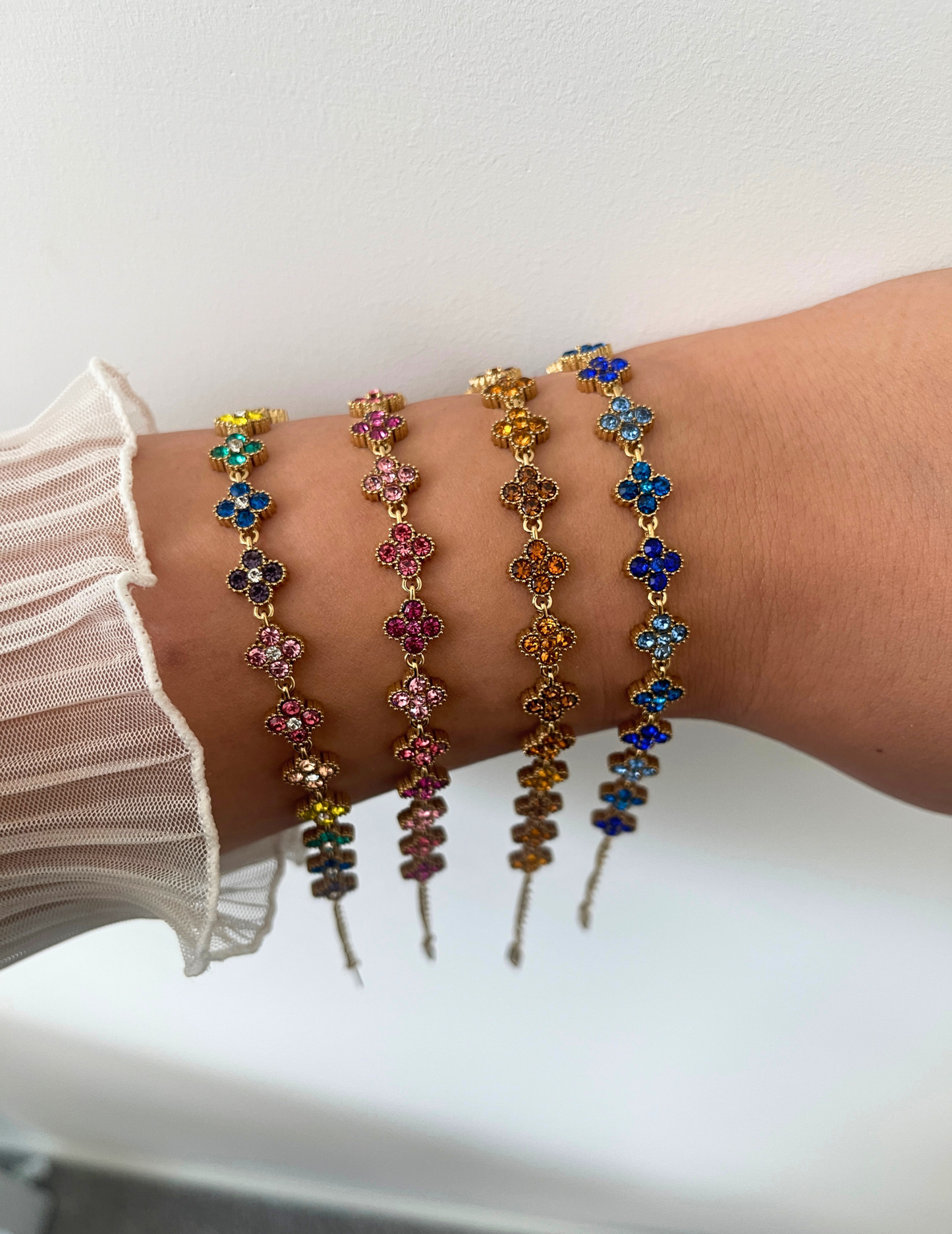 wrist wearing four colorful clover bracelets on neutral background