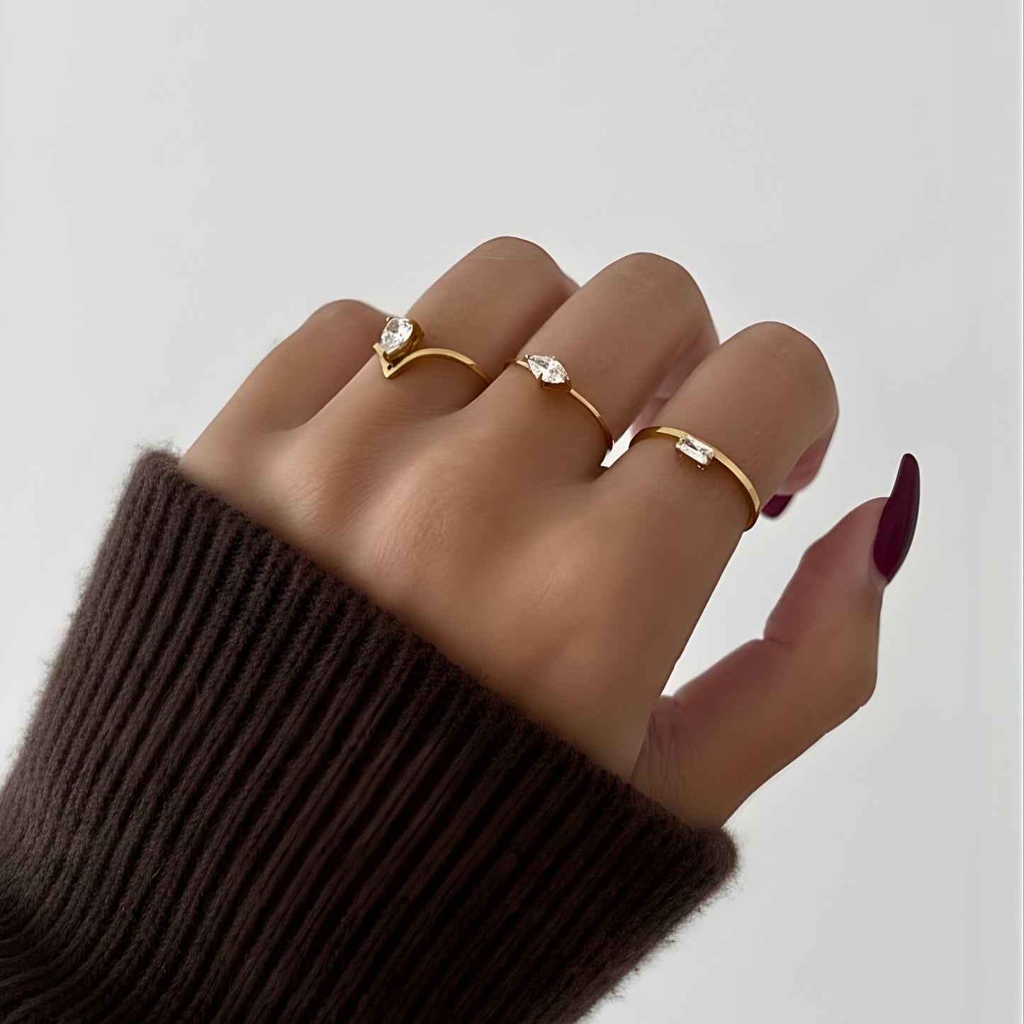 Hand wearing three gold rings with gemstones on a plain background