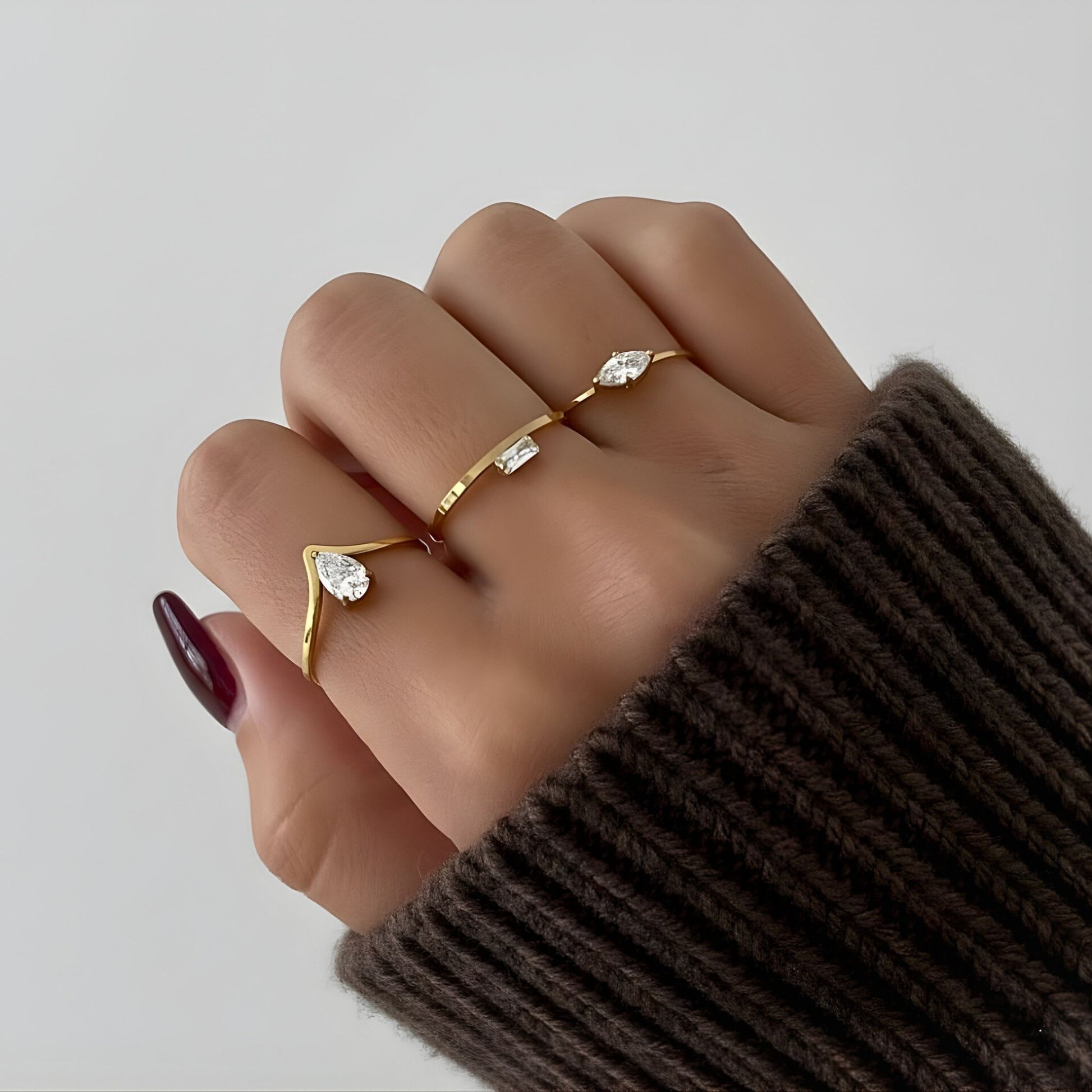 Hand wearing gold rings with gemstones on a neutral background