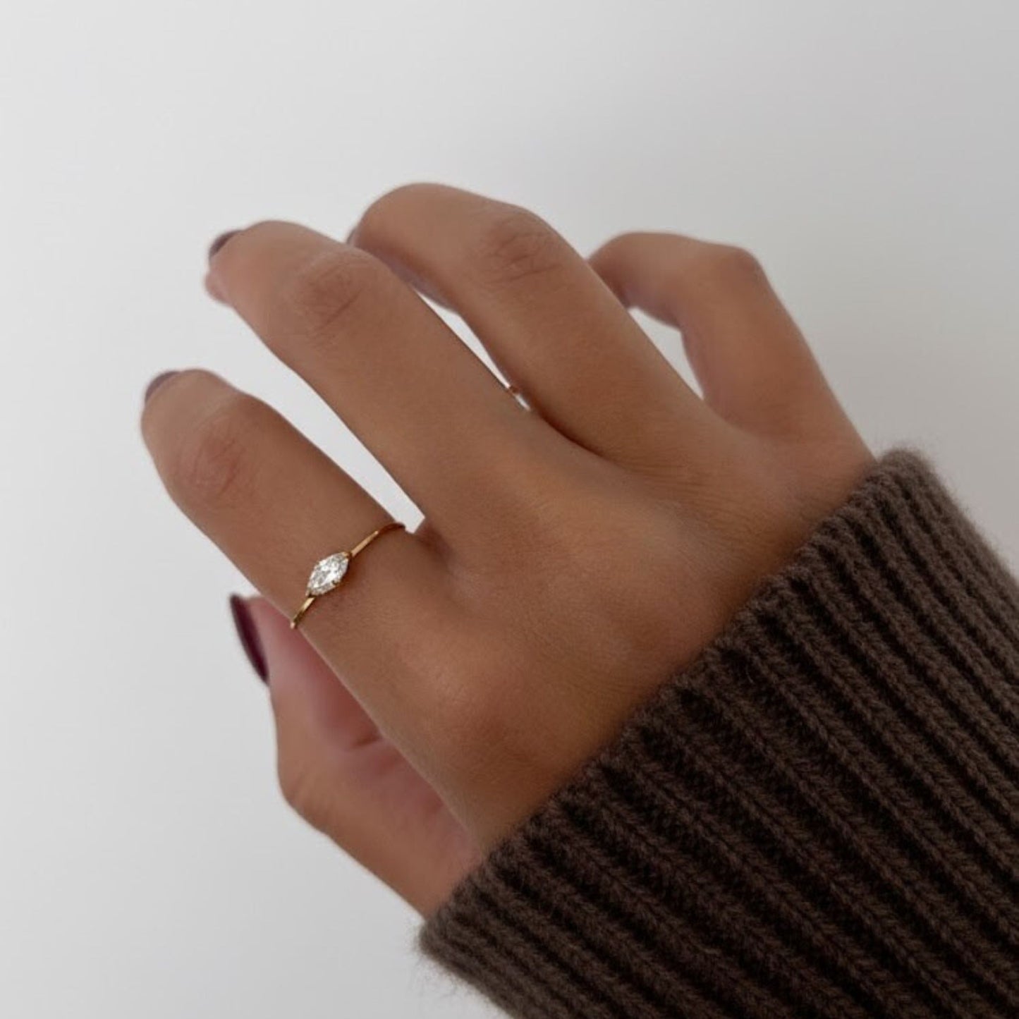 Hand wearing a gold ring on a plain background