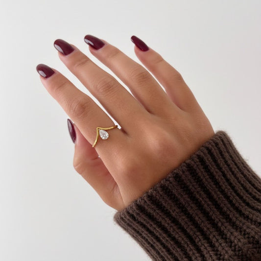 Hand wearing a gold ring with a diamond on a plain background