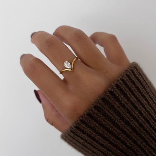 Hand wearing a gold ring with a diamond on a plain background