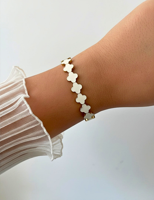 Wrist wearing a white clover bangle on a neutral background.